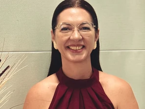 Dra. Cíntia Urquiza sorrindo, sentada no consultório, de blusa vinho